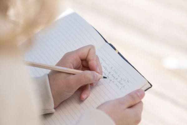 Femme en train d'écrire dehors sur un banc.
