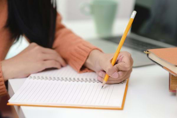 Femme concentrée écrivant dans un cahier à un bureau.