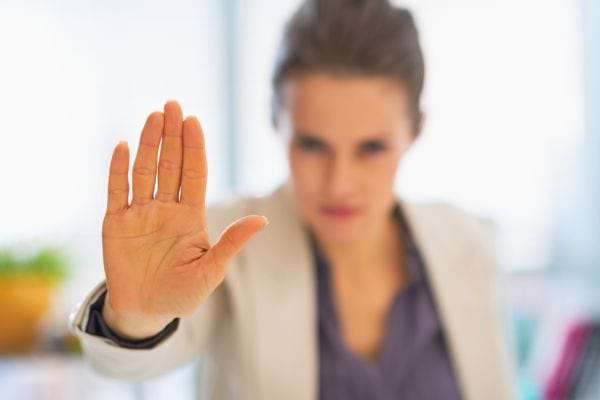 Une femme au bureau tend la main vers la caméra en signe de stop, visage sérieux.