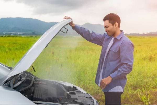 Homme inspectant un moteur de voiture ouvert.