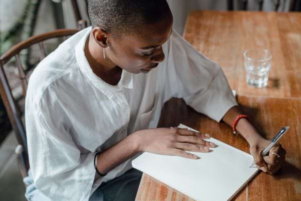 Homme noir écrivant dans un cahier à une table.
