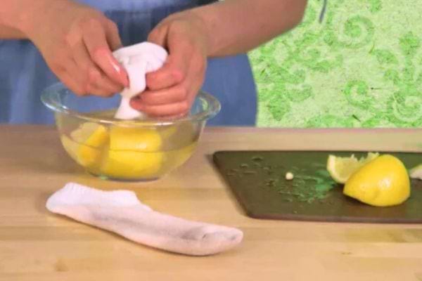 Mains essorant un linge sur des citrons dans un bol.