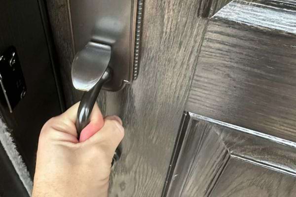 Main ouvrant une porte noire par sa poignée moderne.