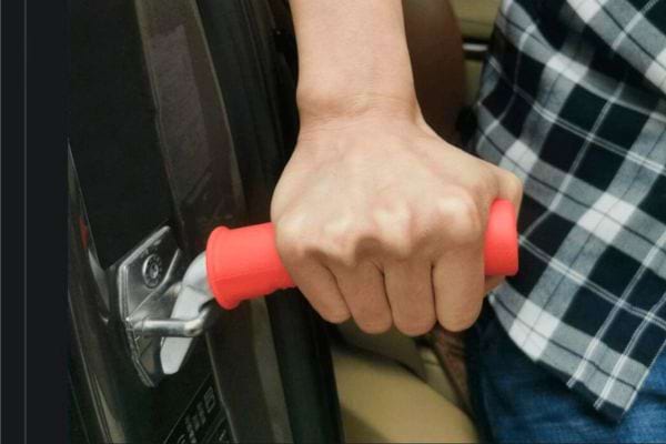 Une main saisit une poignée rouge attachée au crochet de la portière d'une voiture.