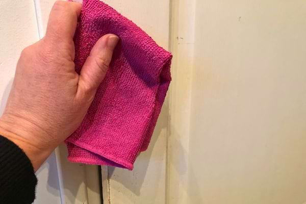 Une main essuyant une porte blanche avec un chiffon rose.