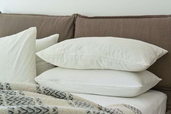 Oreillers blancs empilés sur un canapé marron.