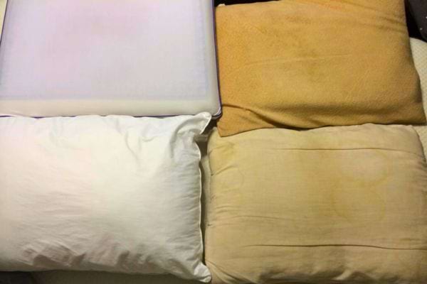 Assortiment d'oreillers, dont certains jaunis, sur un lit.