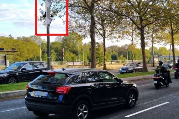 Radar sur un pôle au bord d'une route urbaine, voitures et motos passant.