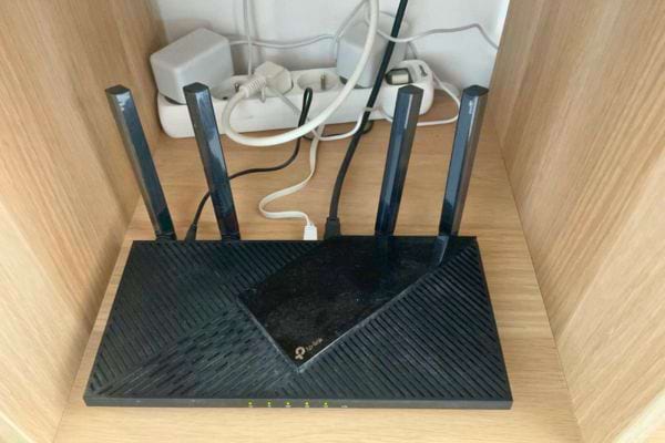 Routeur sans fil avec six antennes sur une étagère en bois, entouré de câbles.