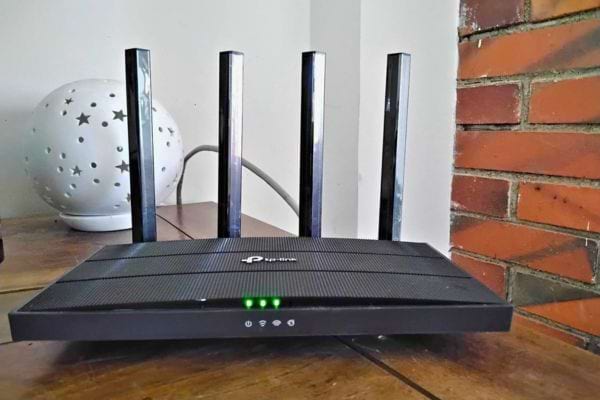 Routeur noir sur un sol en bois, près d'un mur en briques, avec quatre antennes.