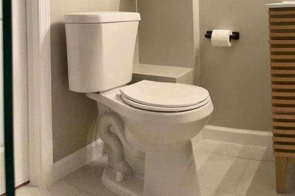 Toilette blanche dans un coin d'une pièce éclairée, à côté d'un rouleau de papier.