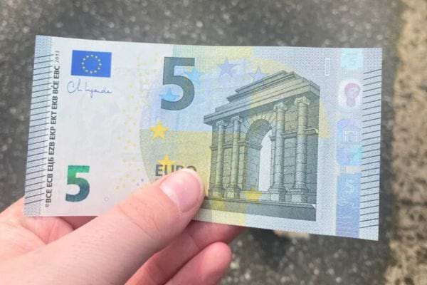 Un billet de cinq euros tenu dans une main.