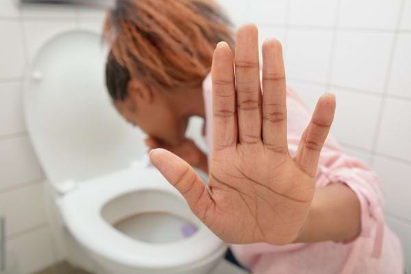 Femme se tenant l'estomac, malade près des toilettes.