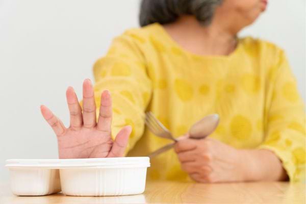 Une femme âgée refusant un contenant de nourriture.