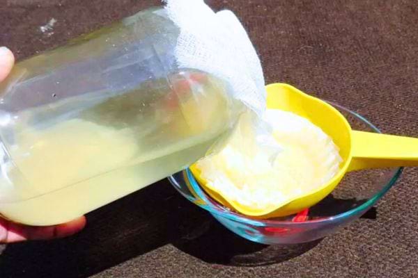 Une main qui filtre un bocal de vinaigre blanc maison avec de l'étamine et un filtre café. 