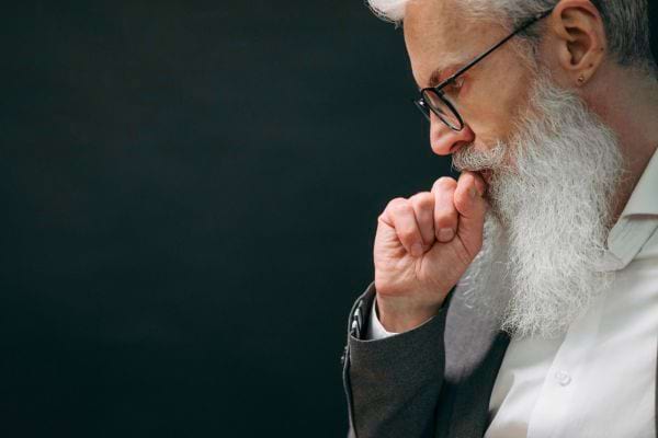 Homme âgé avec une longue barbe blanche et lunettes, pensif, main sur le menton.