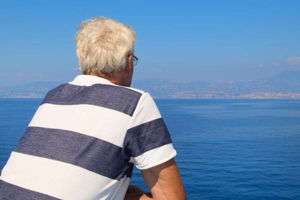Homme âgé de dos, regardant la mer, portant un t-shirt rayé blanc et bleu.