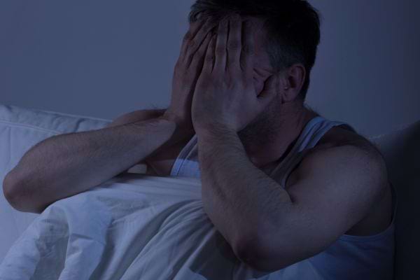 Homme assis dans le noir, se tenant la tête dans les mains.