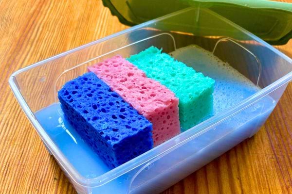 Des lingettes sèche-linge maison dans une boîte Tupperware sur une table en bois.