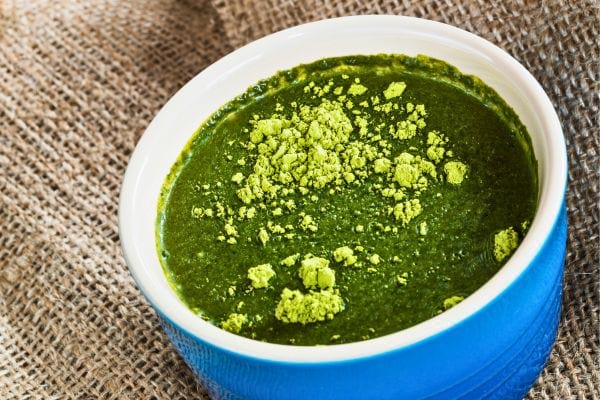 soupe de moringa verte garnie de poudre dans un bol bleu.
