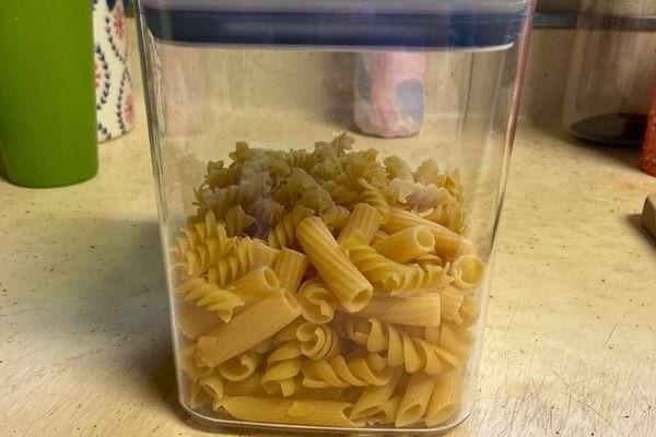 Un bocal en plastique rempli de divers types de pâtes sèches sur un plan de travail de cuisine.