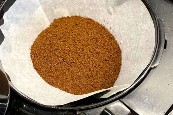 Du café moulu dans un filtre en papier blanc reposant sur une cafetière.