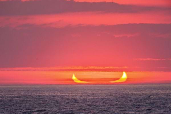 Horizon marin avec éclipse créant une image de cornes sur un ciel rosé.