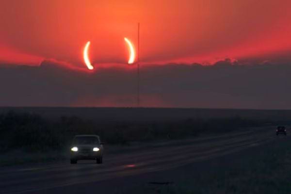 Voiture roulant sur une route avec une éclipse formant des "cornes du diable" au crépuscule.