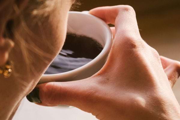 Une femme tient une tasse de café noire près de son visage pour boire.
