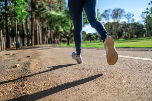 Femme en tenue de sport, courant sur un chemin bordé d'arbres.