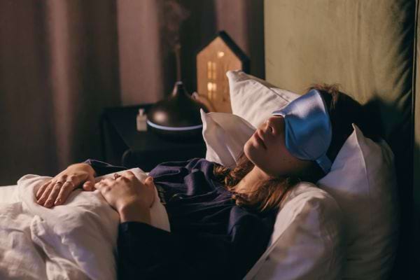 Femme portant un masque de sommeil, allongée sur un lit.