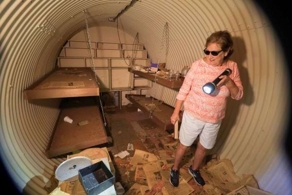 Une femme explore un abri antiatomique désordonné, équipé d'une lampe de poche.