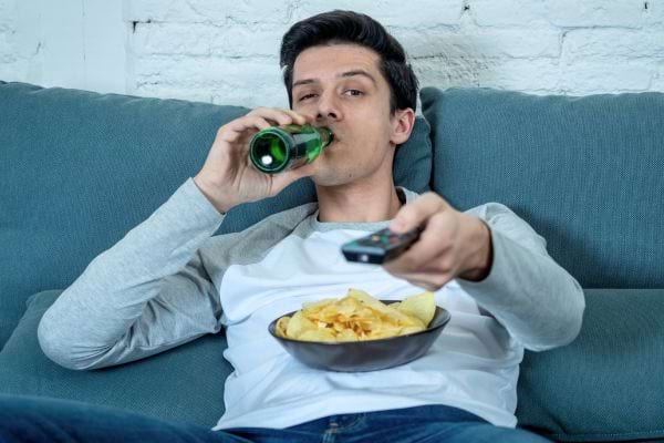Un homme sur un canapé buvant de la bière et mangeant des chips.