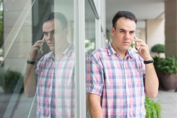 Un homme parle au téléphone à côté d'une vitre reflétante.