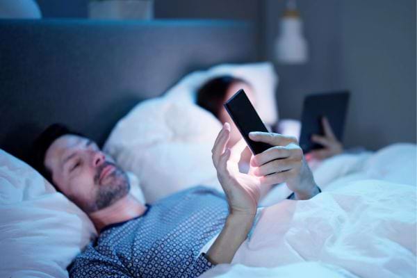 Homme sur son lit, regardant son téléphone de nuit.