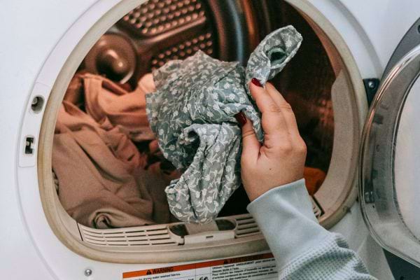 Une main féminine retire un vêtement d'une sécheuse.