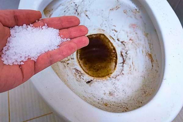 Main tenant du sel au-dessus d'une cuvette très sale.