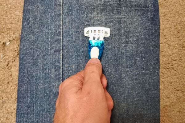 Main tenant un rasoir sur un jean.