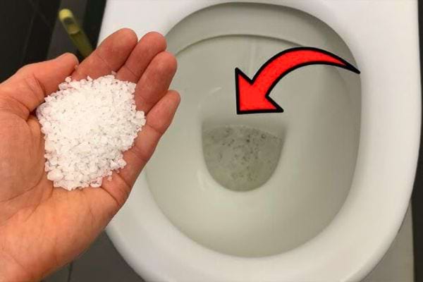 Main tenant du gros sel au-dessus d'une cuvette de toilette.