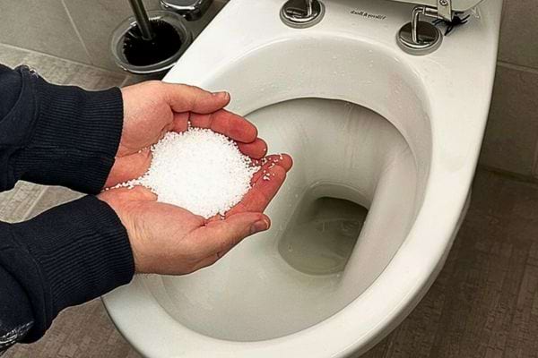 Main versant du sel dans une cuvette de toilettes publiques.
