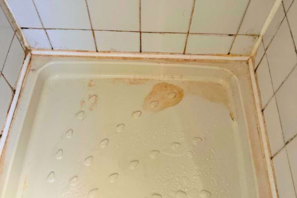 Baignoire blanche avec des moisissures roses sur les joints et au coin des carreaux.