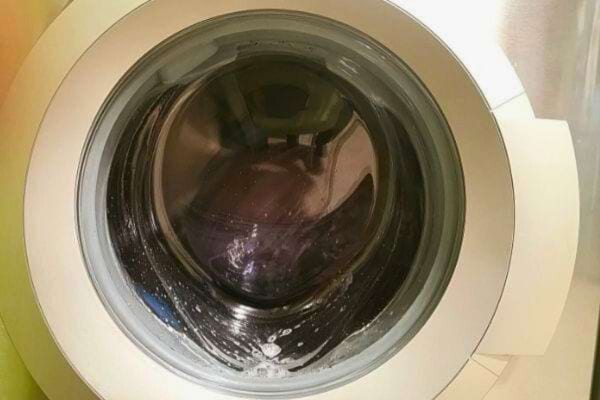 Porte d'une machine à laver fermée avec de la mousse visible sur le hublot.