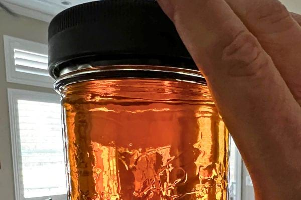 Un pot de verre contenant de l'huile de lin, tenu à la main.