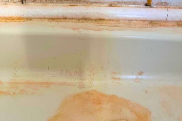 Baignoire ancienne avec des taches et traces roses le long du rebord.