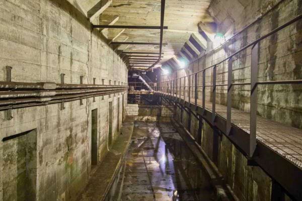 Un long tunnel sombre et humide avec des rails et des lumières au plafond.