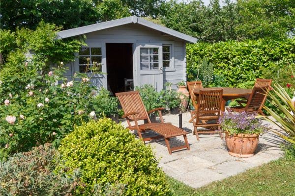 Abri de jardin gris entouré de fleurs avec salon en bois.