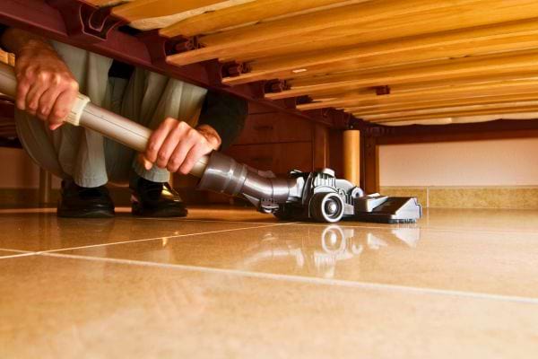 Personne passe l’aspirateur sous un lit en bois.