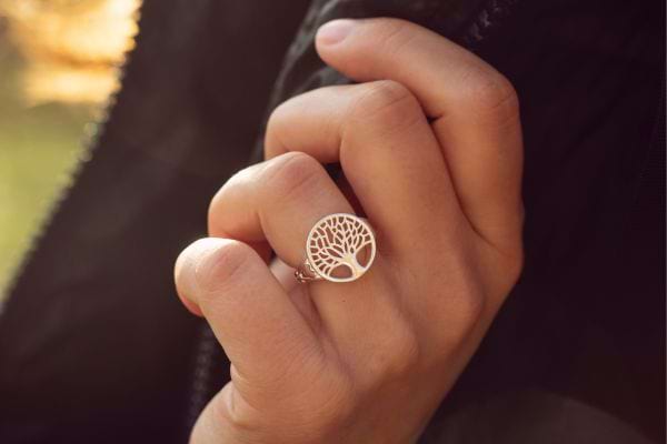 Main tenant un manteau avec une bague arbre de vie au design ajouré.