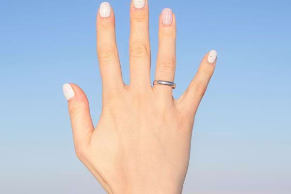Main levée vers le ciel portant une fine bague argentée sur l’annulaire droit.