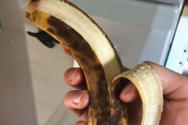 Banane très mûre à moitié pelée dans une main.